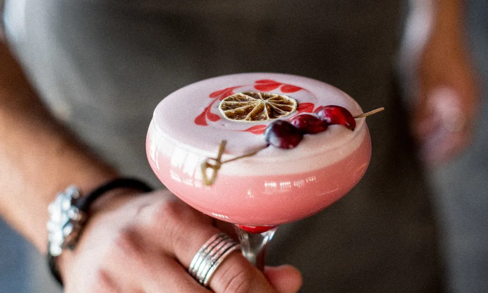 Pink cocktail in martini glass topped with blood orange and cherries.