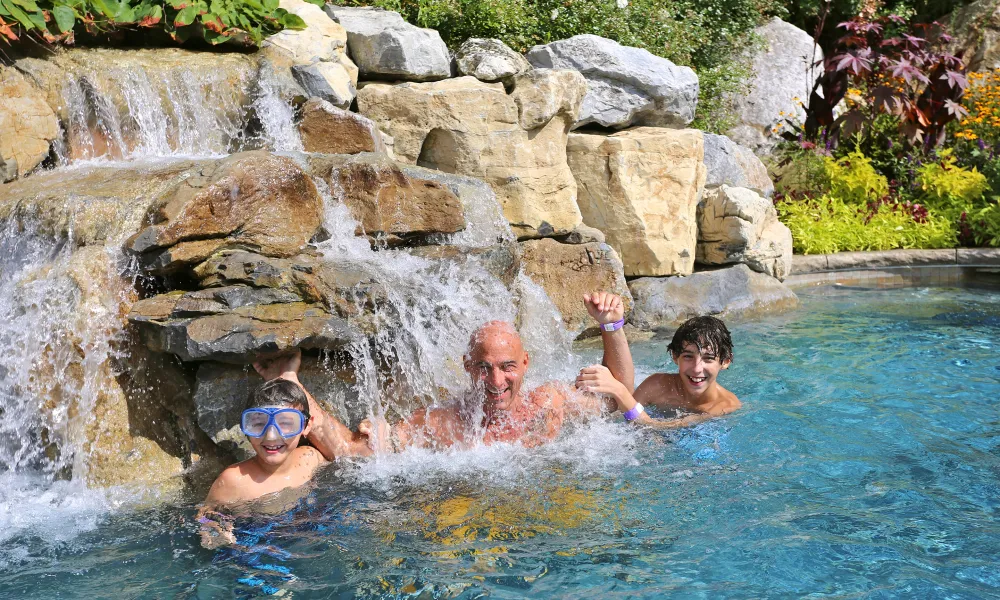 Childrean and father underneath waterfall in outdoor Biosphere pool.