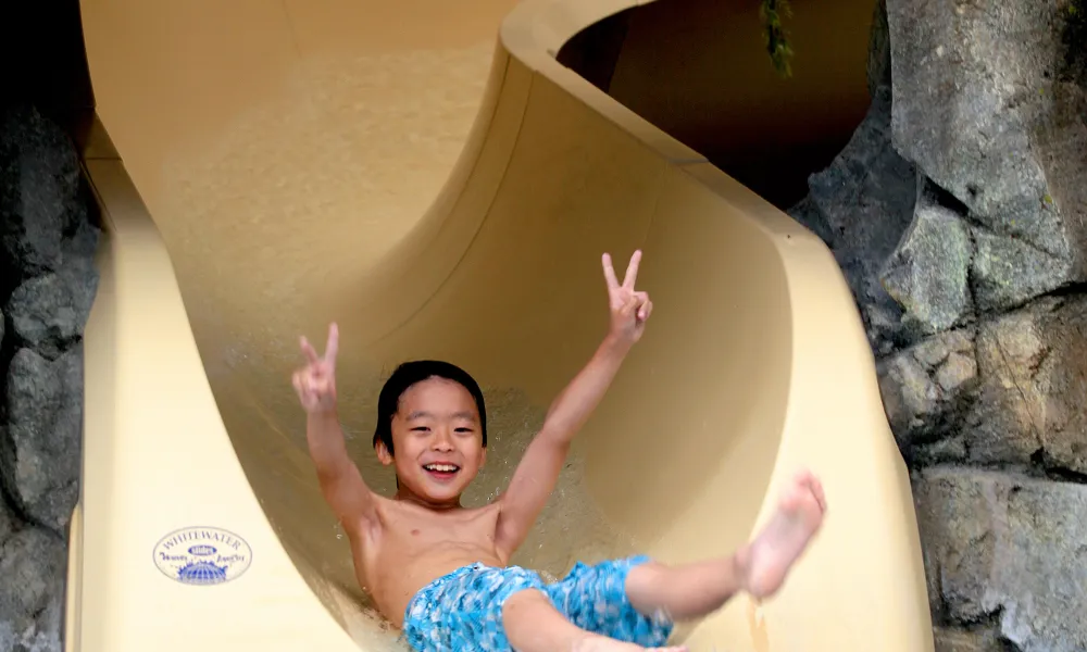 Children showing peace signs on his hands as he slides down Biosphere indoor slide.