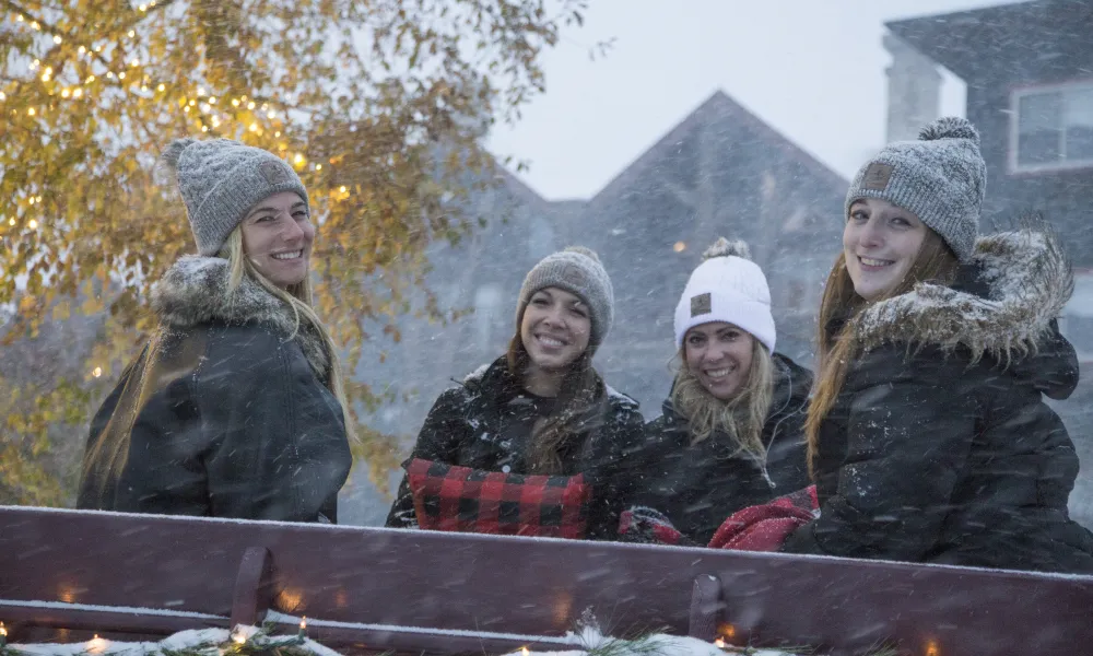 Four girlfriends sitting in a carriage while it's snowing.