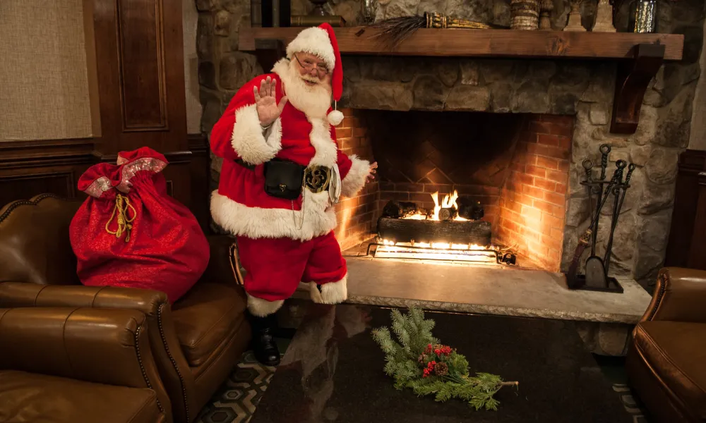 Santa standing by the fireplace in Grand Cascades Lodge.