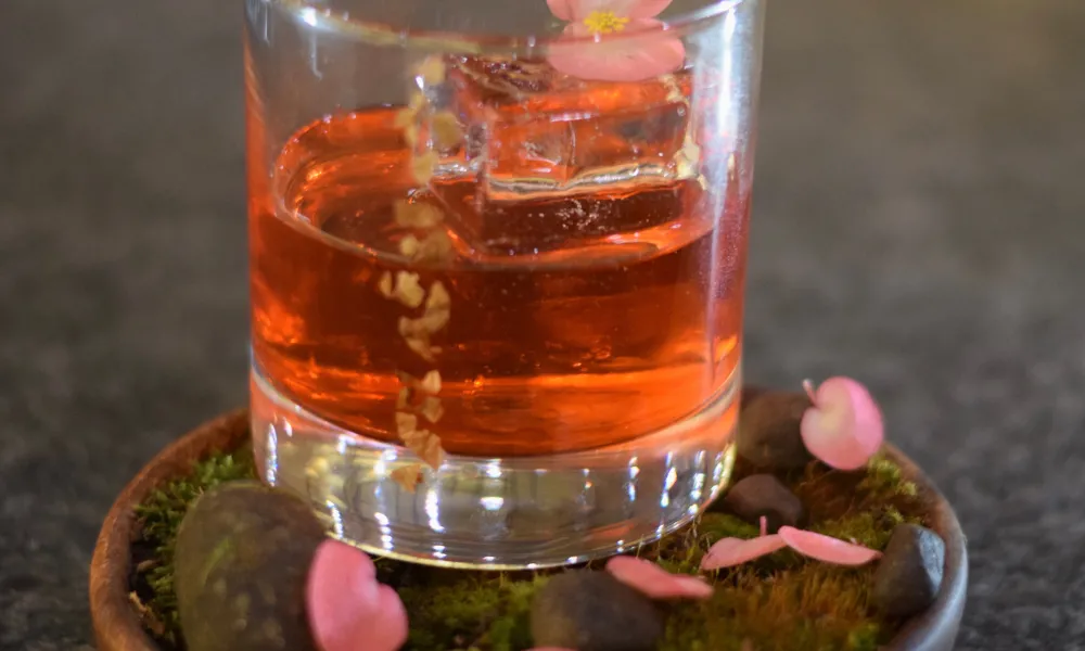 Short round glass filled with pink cocktail and flower petals.