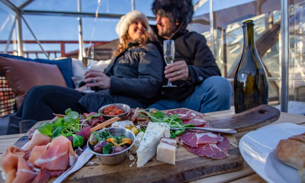 Couple sitting in champagne chalet enjoying charcuterie board.