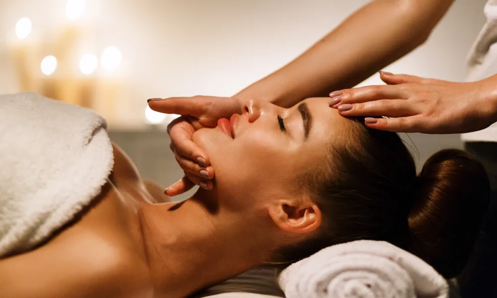 Woman laying on table with facialists hands on her chin and forehead. 