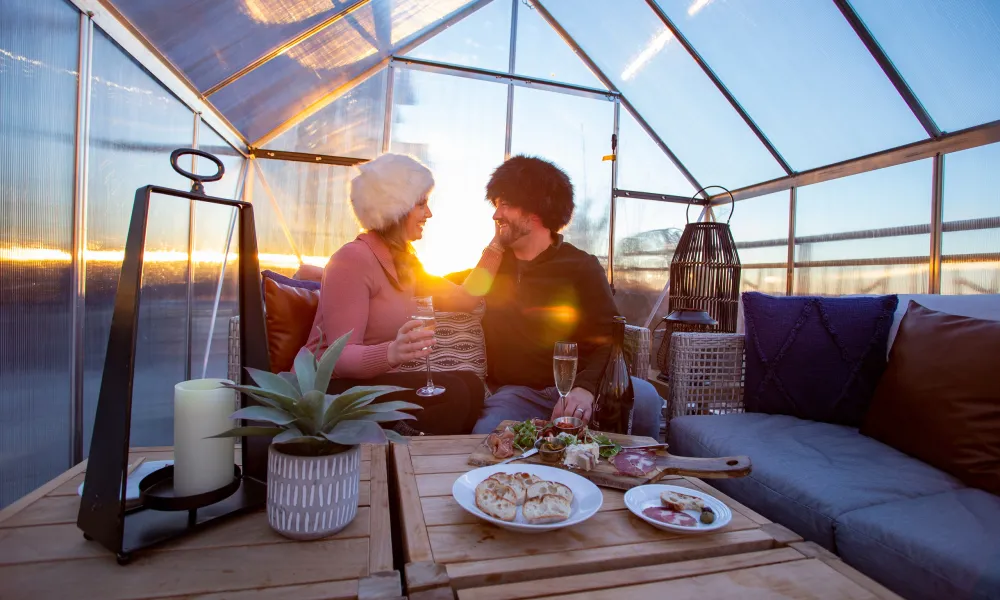 Couple in fuzzy hats drinking champagne in chalets.