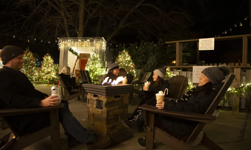 Family of four drinking festive drinks around fire at Frosty's Cantina.