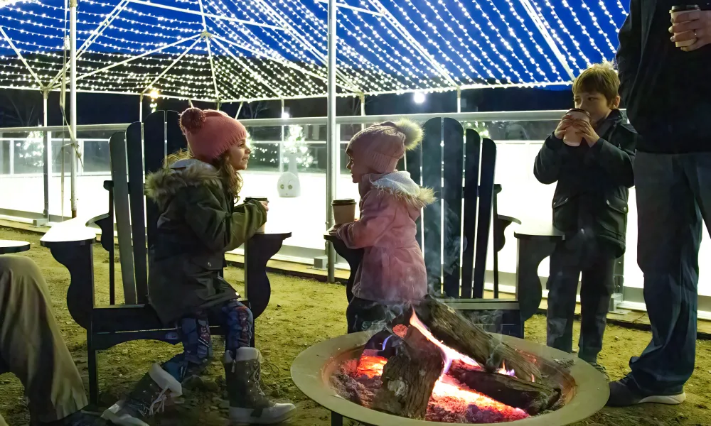 Two children sitting by firepit with hot chocolate.