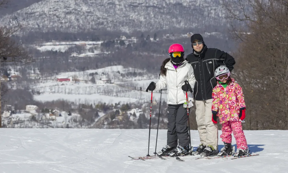 Family of 3 skiiers standing on mountain.