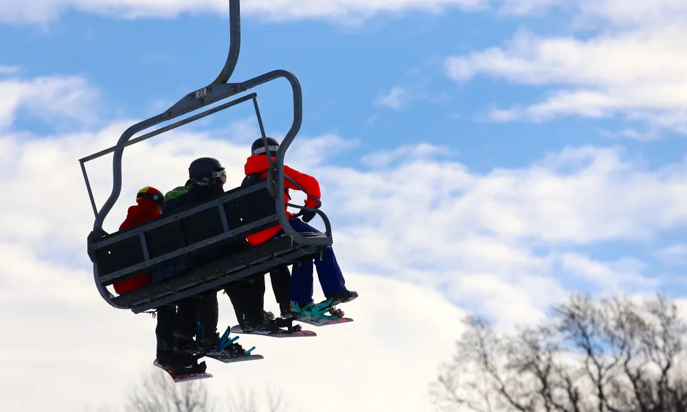 Three people sitting on ski lift.