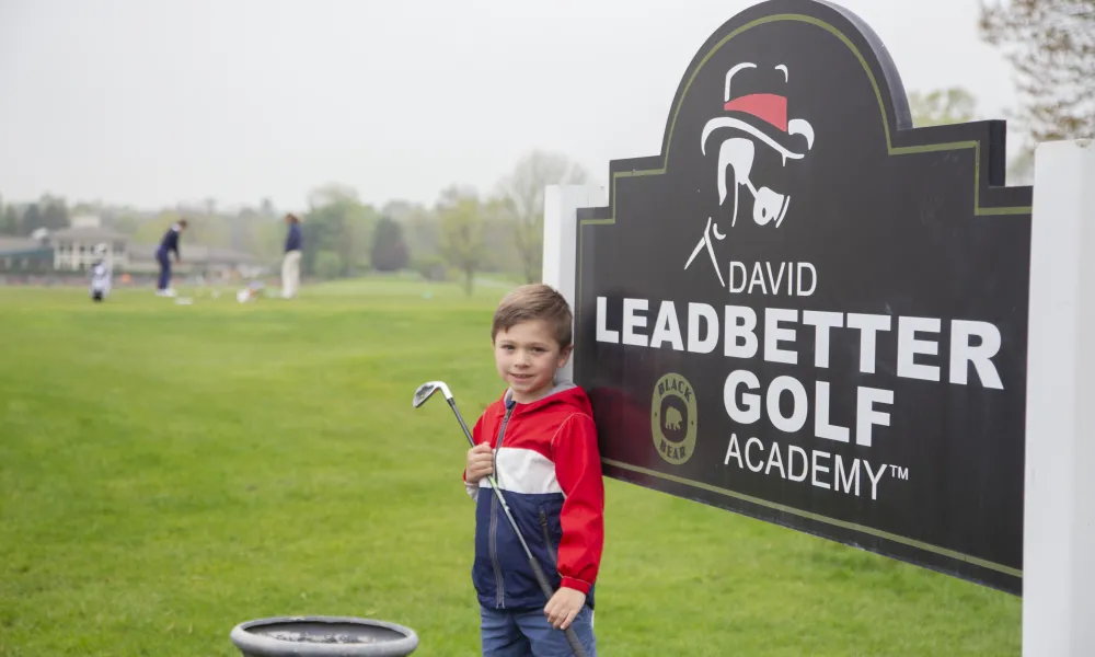 Young boy standing in front of the Leadbetter Golf Academy sign