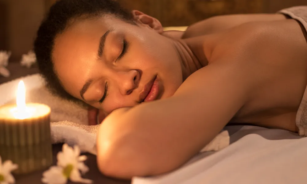 Woman laying on spa table surrounded by little candles.