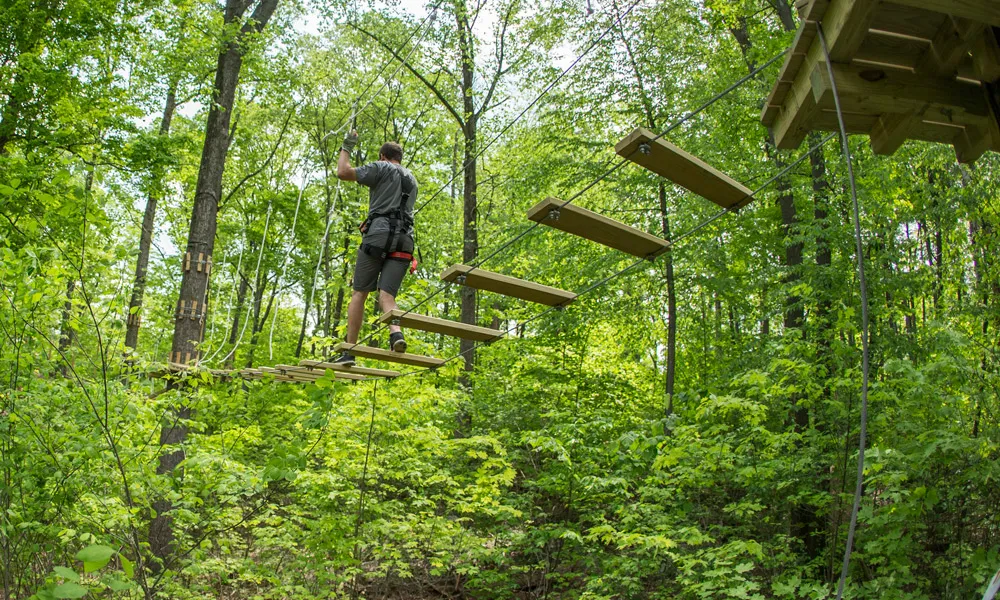 Man walking on wooden slats in tree ropes course.