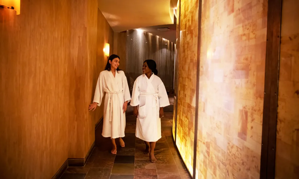 Two women in white bathrobes walking down Elements Spa hallway.