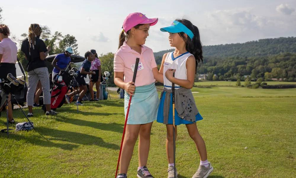 Two girls smiling at each other, learning to golf at Crystal Springs Resort