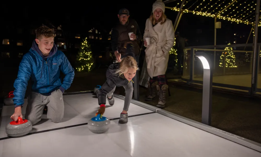 Boy and girl about to push curling stone down ice.