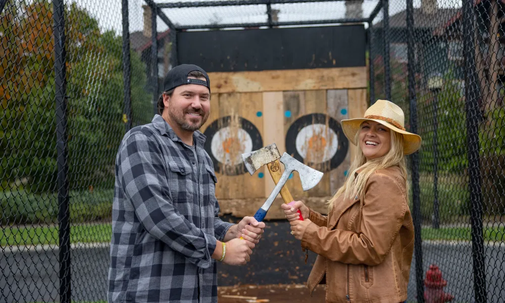 Woman and man holding axes in front of axe throwing target during couples getaway.