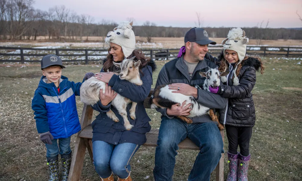 Family of four bundled up in winter clothing and holding baby goats.