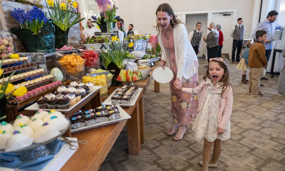 Woman and child holding hands and looking at buffet of food. 