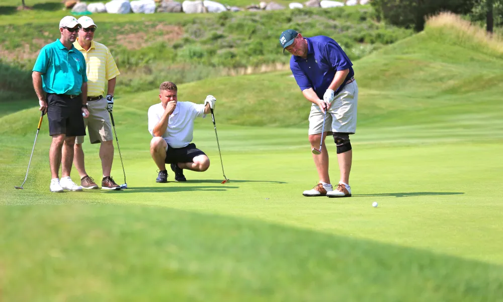 A foursome of guys on the putting green of a golf course at Crystal Springs Resort