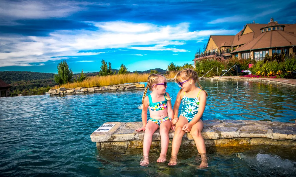 Two young girls wearing sunglasses and sitting at the Vista 180 pool.