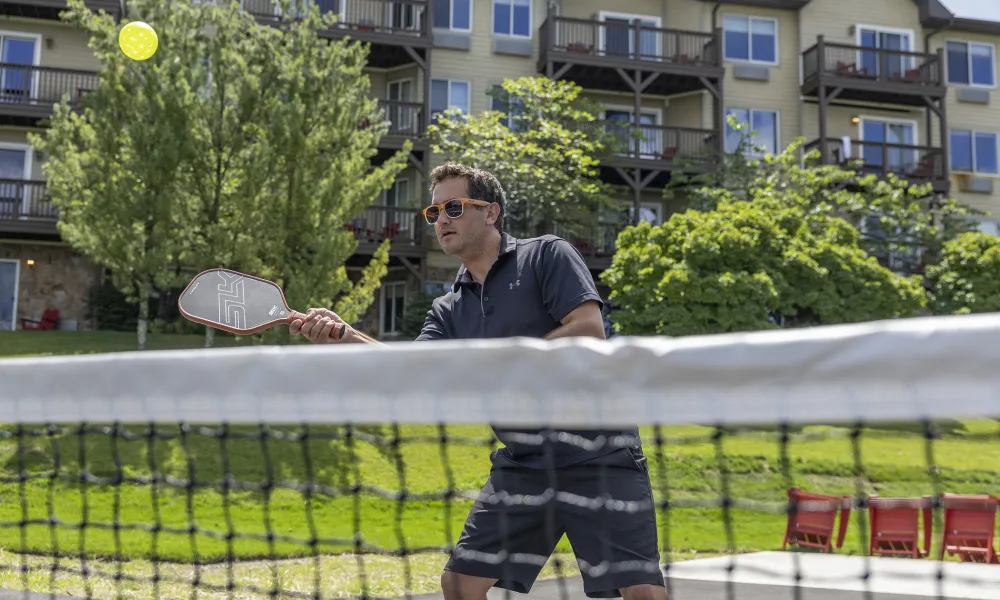 Man hitting ball over pickleball net.