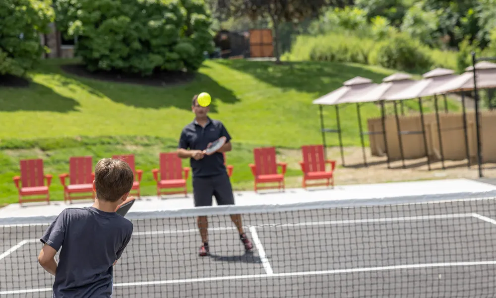 Child playing pickleball with father.