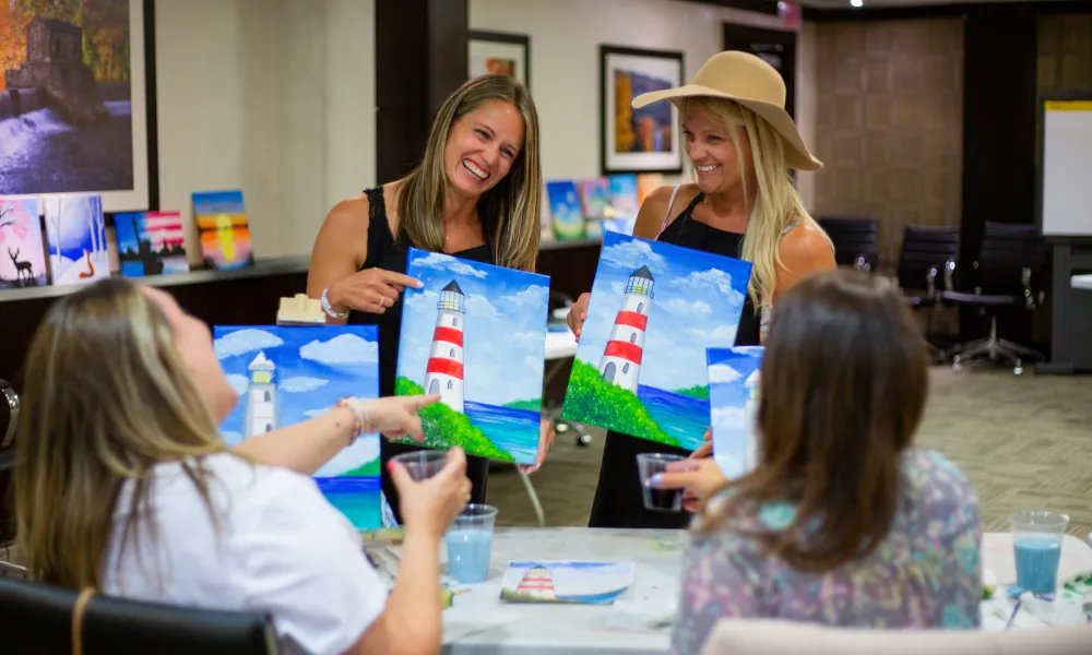 Four girlfriends showing their lighthouse painting from the Paint &amp; Sip activity.