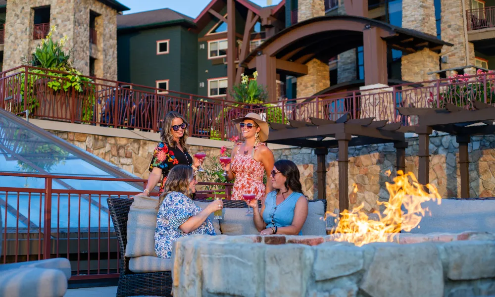 Group of four girlfriends sitting around firepit on Fire &amp; Water terrace.