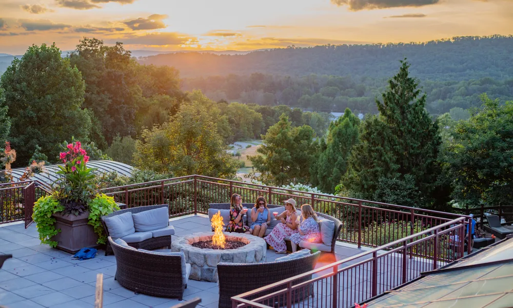 Group of four girlfriends sitting around firepit on Fire &amp; Water terrace overlooking sunset mountain views.