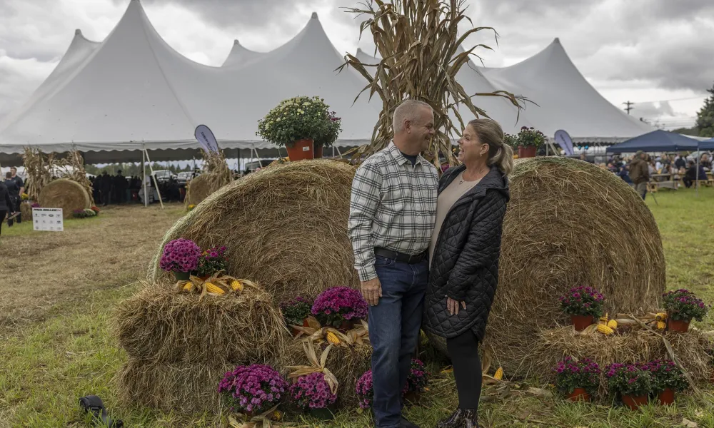 Couple standing in front of two large hay bales.