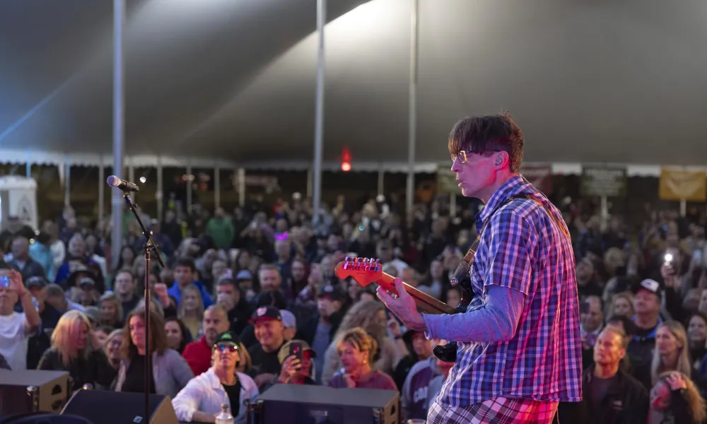 Man playing guiatr on music fest stage with large crowd in front of him