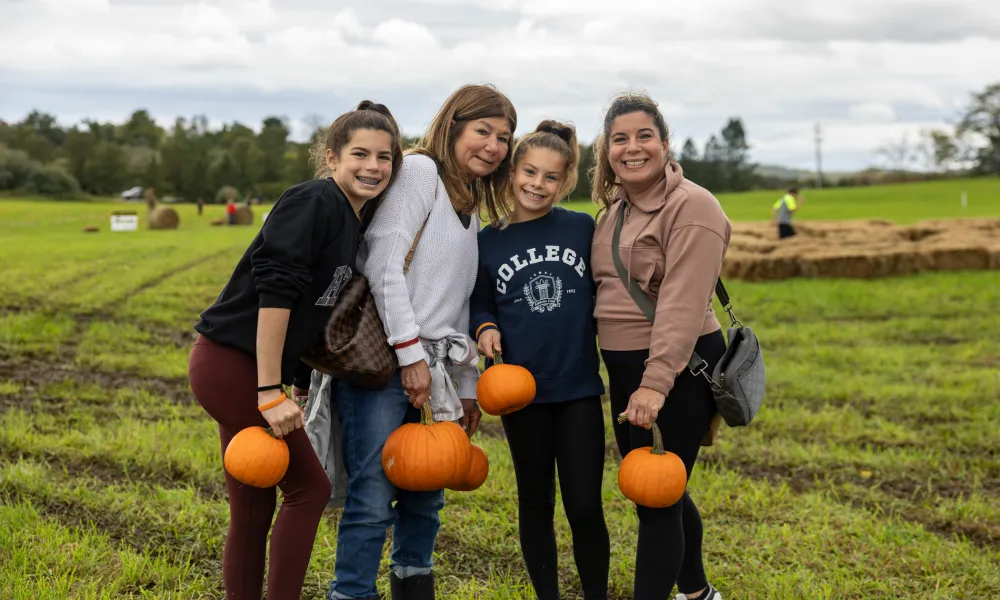 Two women and two children standing in an open field holding pumpkins.