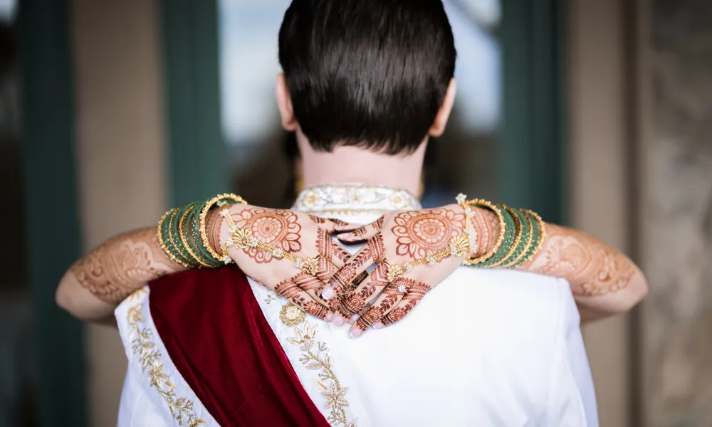 Woman, with henna on her hands, wraps her hands arounds grooms neck.