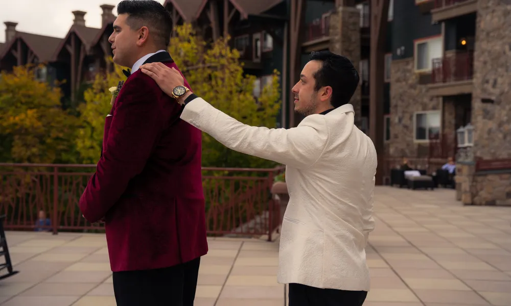 Groom wearing a white jacket, places hand on husbands shoulder during first look.