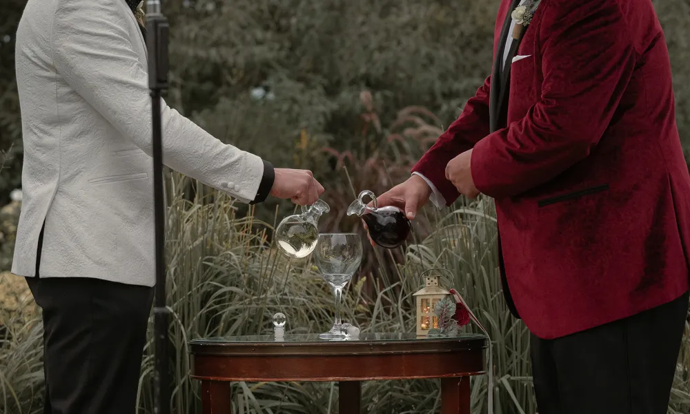 Two grooms pouring wine in glass during ceremony.