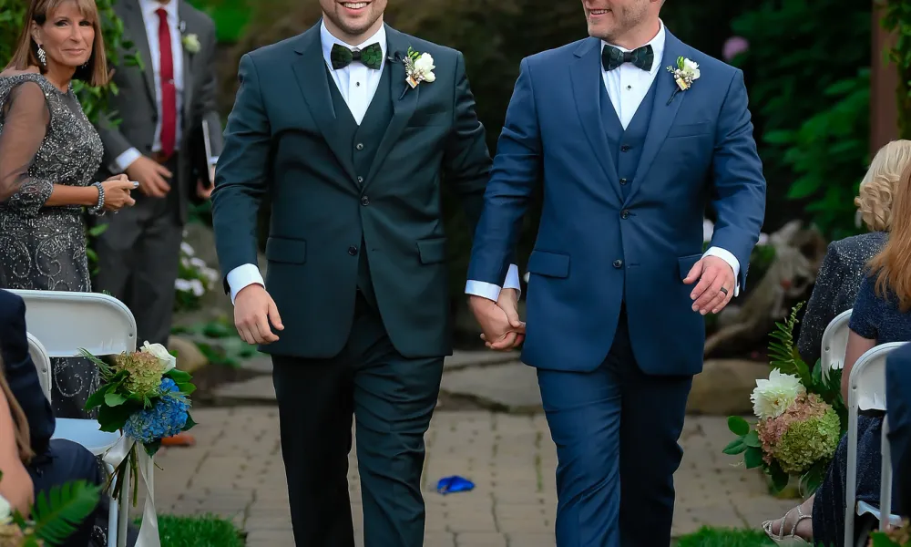 Two grooms, just married, walking hand in hand down the aisle.