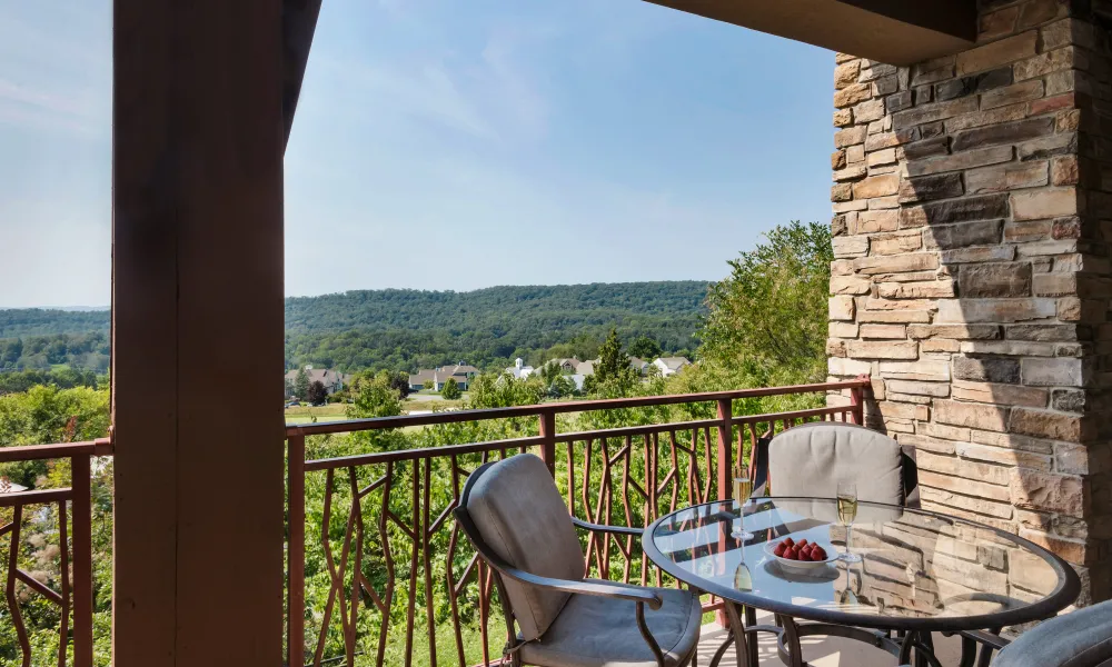 Table and chairs on balcony of Grand Cascades Lodge with mountain view.