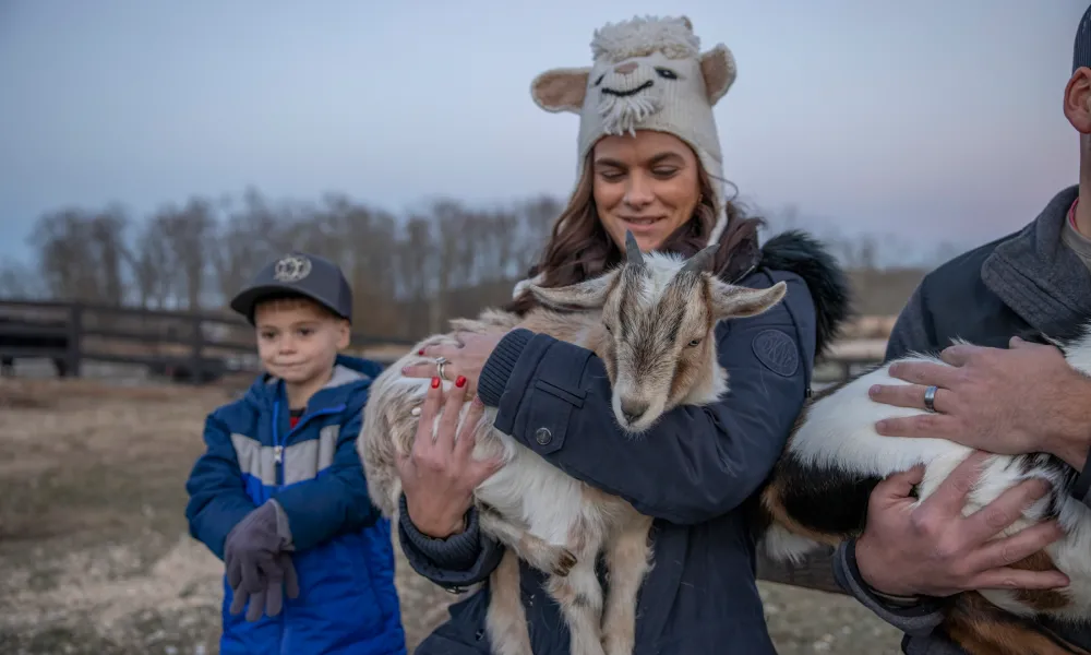 Woman wearing a goat hat holding a baby goat.