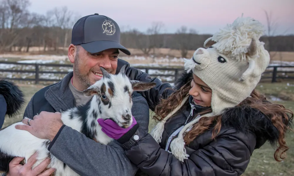 Father and daughter holding baby goat.