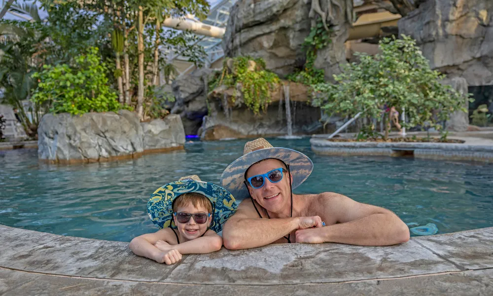 Father and son wearing matching hats and sunglasses in Biosphere pool.