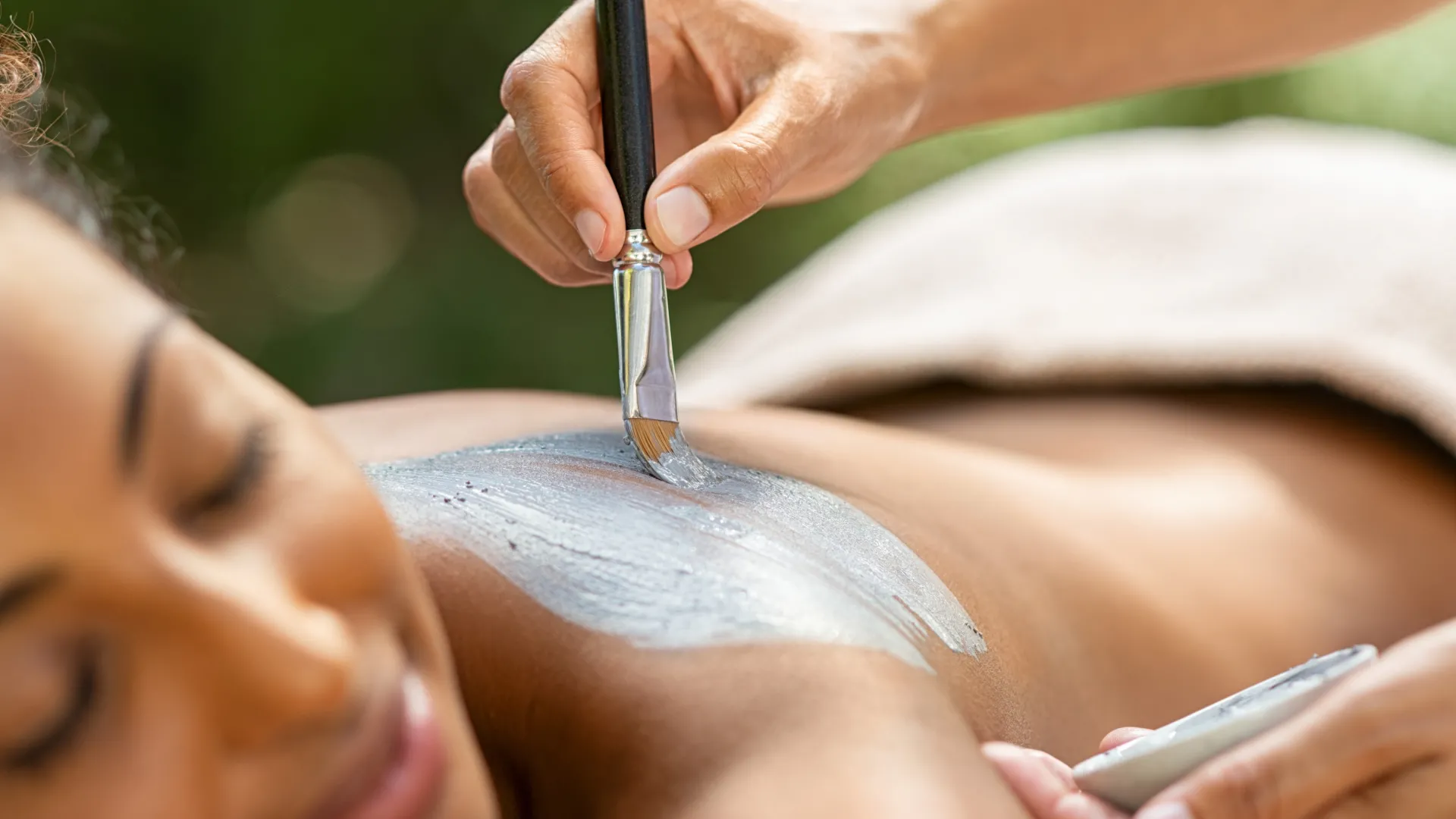 Mud being painted on woman's back for spa treatment.