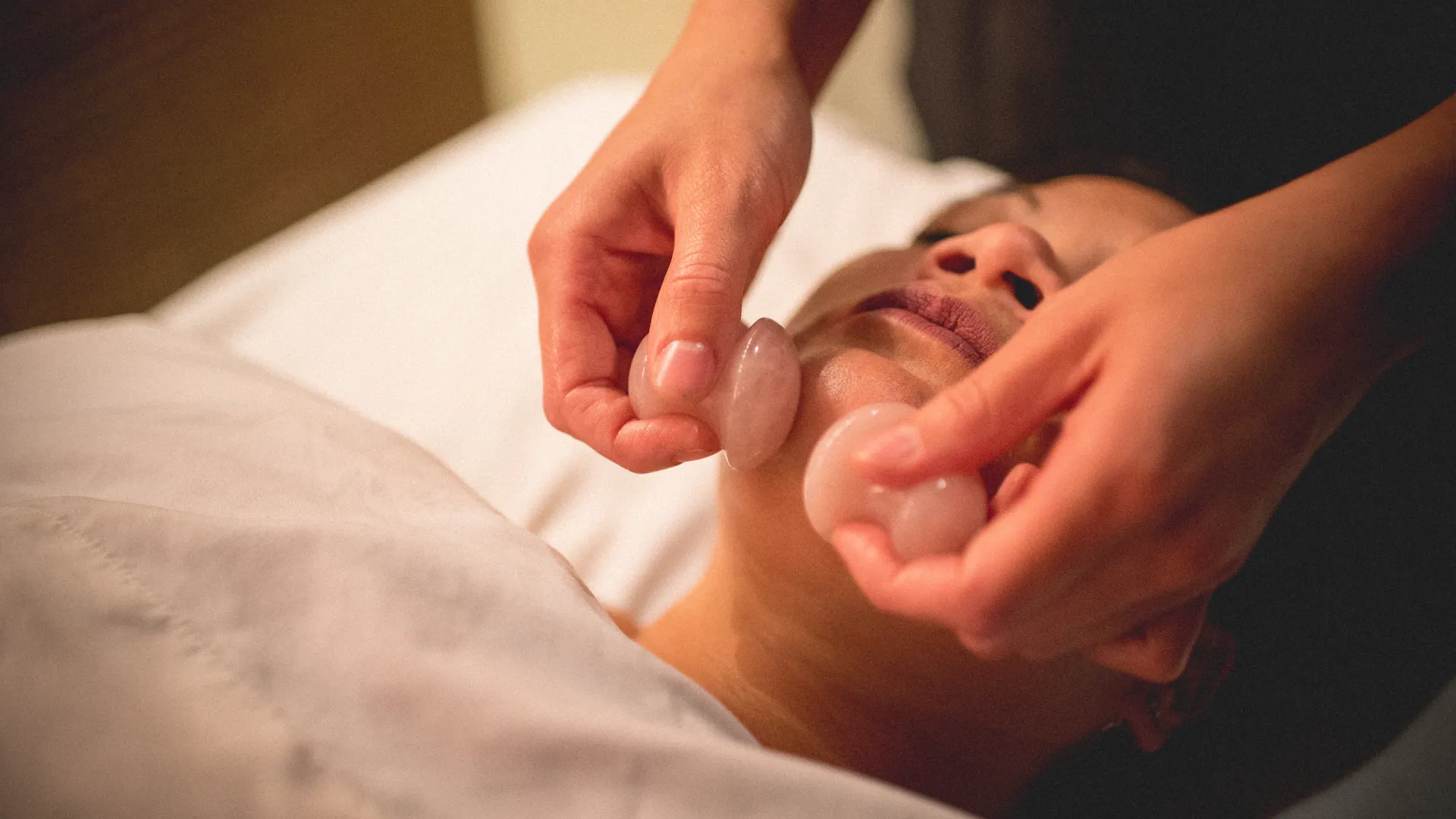 Rose quartz being rubbed on woman's face during facial