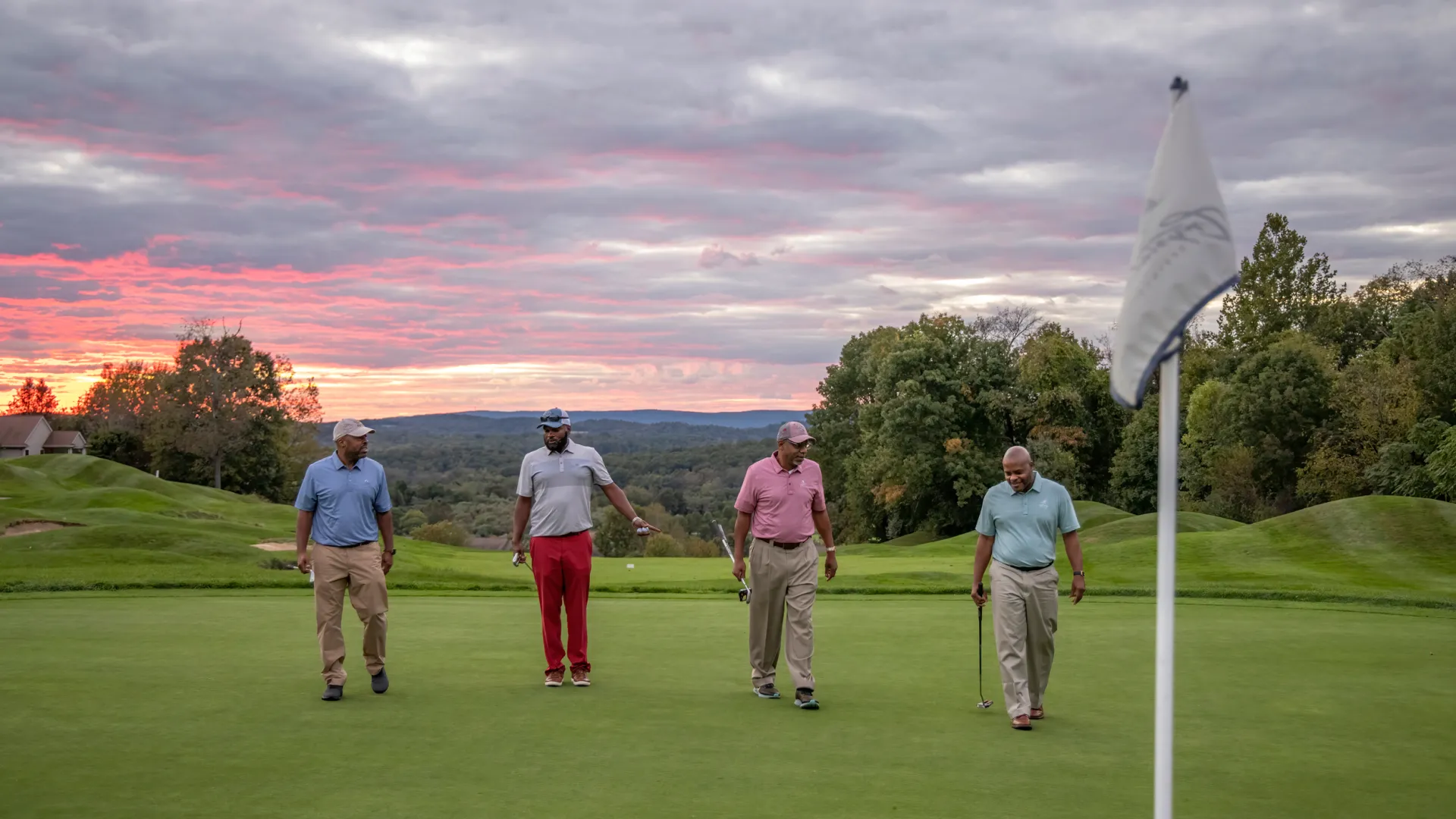 Guys foursome walking on a golf course with the sunset in the background