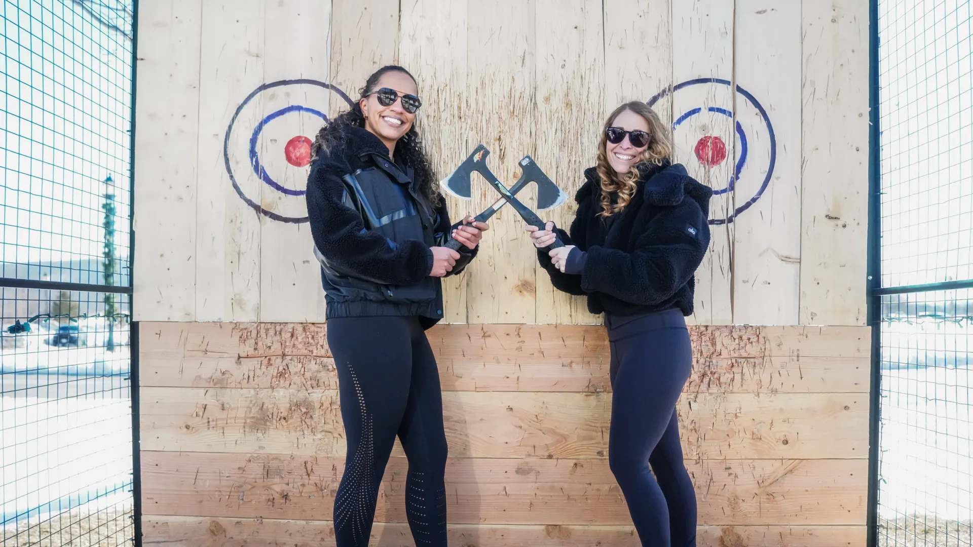 Two women holding axes in front of axe throwing target during girlfriends getaway in NJ.