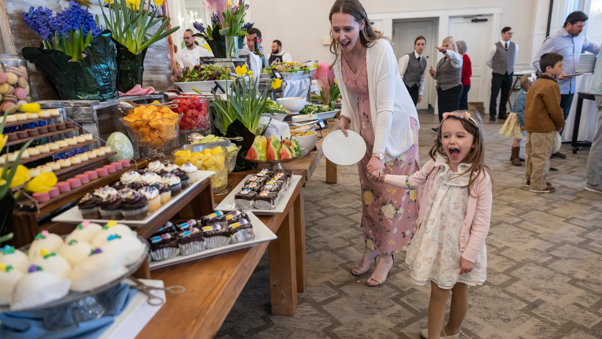 Woman and child holding hands and looking at buffet of food. 