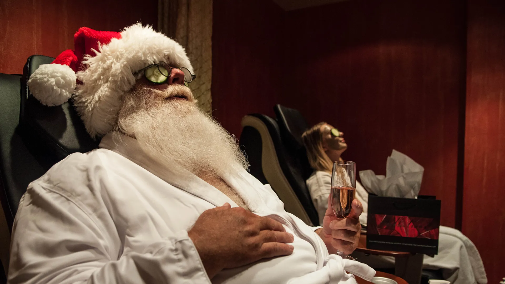 Santa sitting in spa chair holding a glass of bubbles.