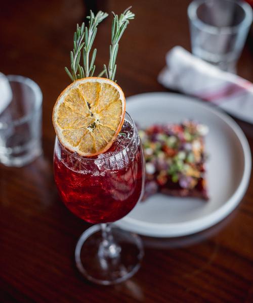 Cocktail topped with rosemary and orange slice.