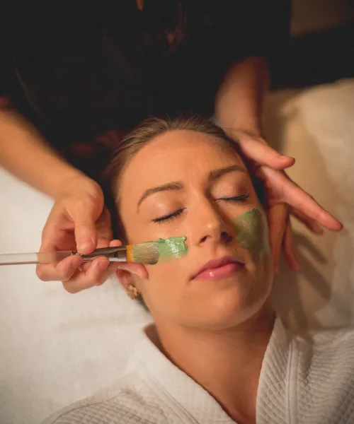 Green face mask being applied to woman's face.