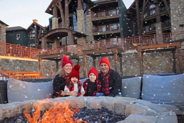 Family of four sits around firepit as it snows around them on Fire & Water Terrace