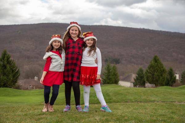 Three girls in holiday outfits posing for a photo with mountains in the background.